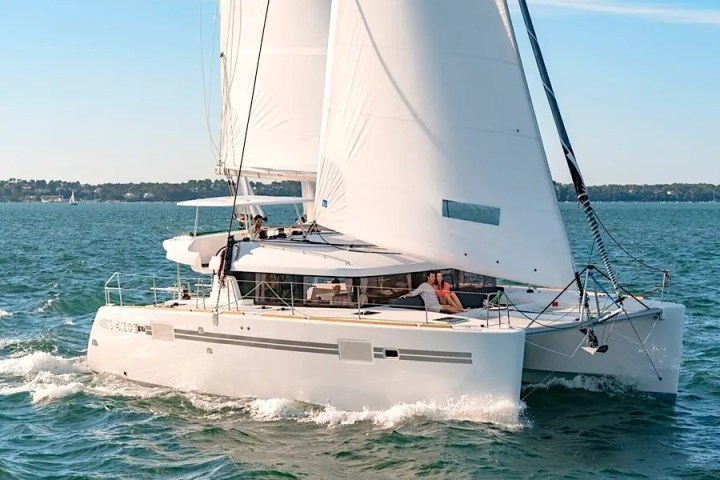 Catamaran with white sails on open water under blue sky.