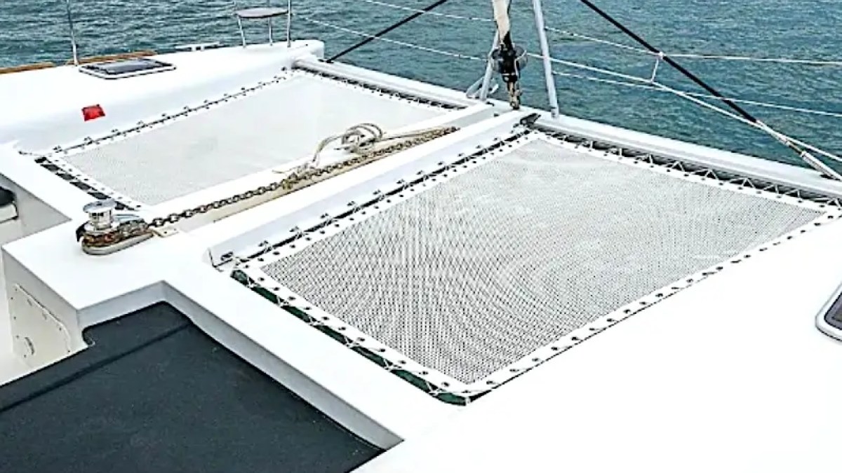 View from a catamaran's deck with netting, overlooking calm ocean waters and cloudy sky.