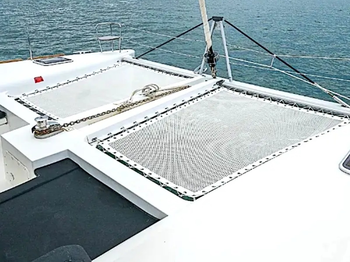 View from a catamaran's deck with netting, overlooking calm ocean waters and cloudy sky.