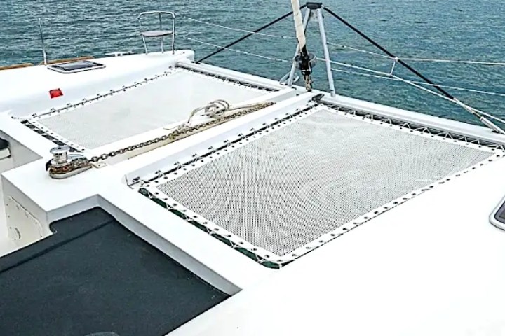 View from a catamaran's deck with netting, overlooking calm ocean waters and cloudy sky.