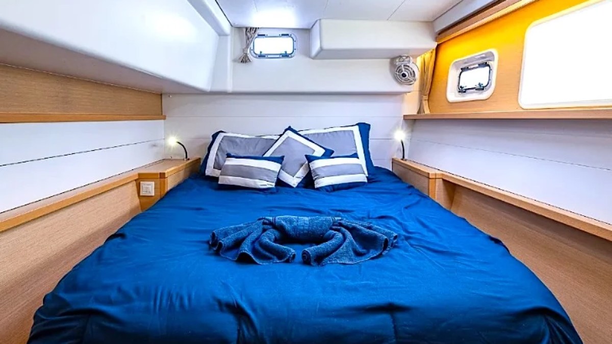 Cozy boat cabin with blue bedding, pillows, and small windows on sides, wood accents, and soft lighting.