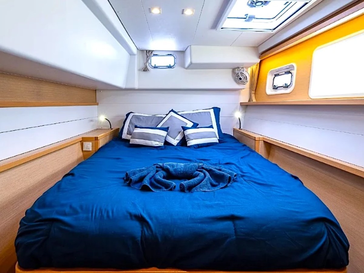 Cozy boat cabin with blue bedding, pillows, and small windows on sides, wood accents, and soft lighting.
