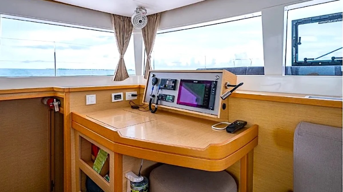 Boat interior with navigation desk, screens, and large windows overlooking the ocean.