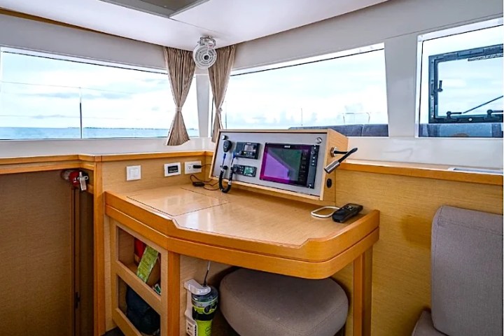 Boat interior with navigation desk, screens, and large windows overlooking the ocean.