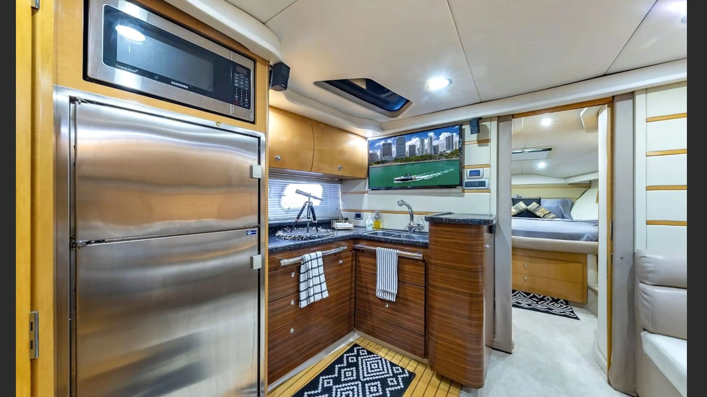 Luxury yacht interior with kitchen, fridge, microwave, and a bedroom in the background.