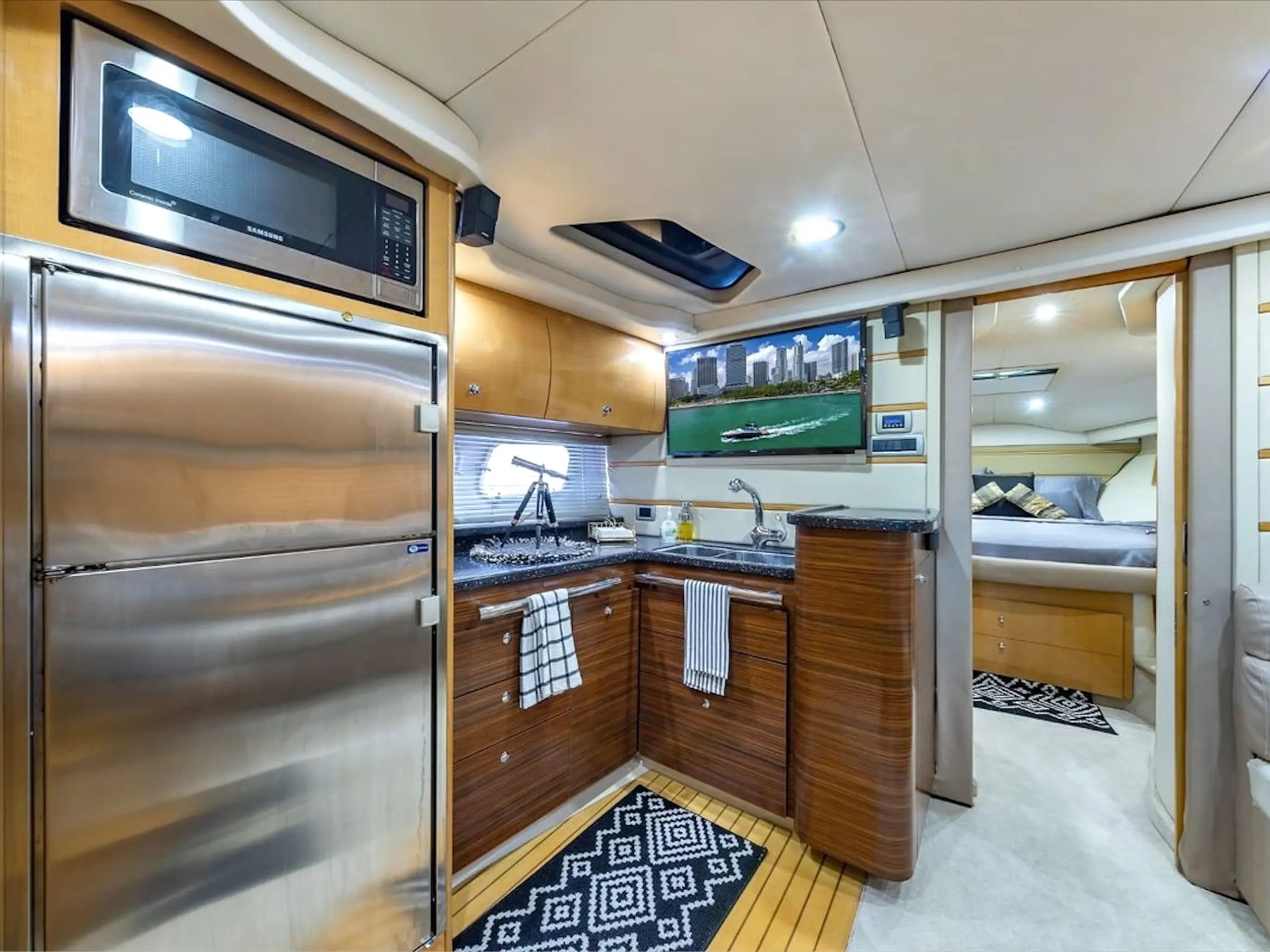 Luxury yacht interior with kitchen, fridge, microwave, and a bedroom in the background.