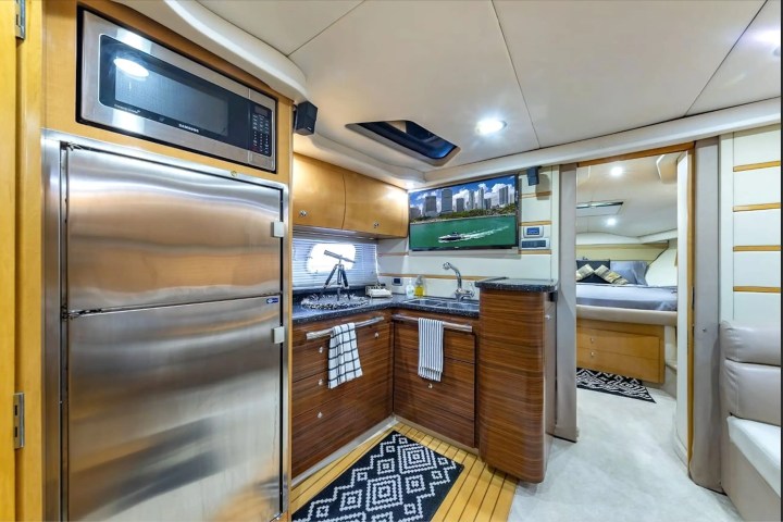 Luxury yacht interior with kitchen, fridge, microwave, and a bedroom in the background.