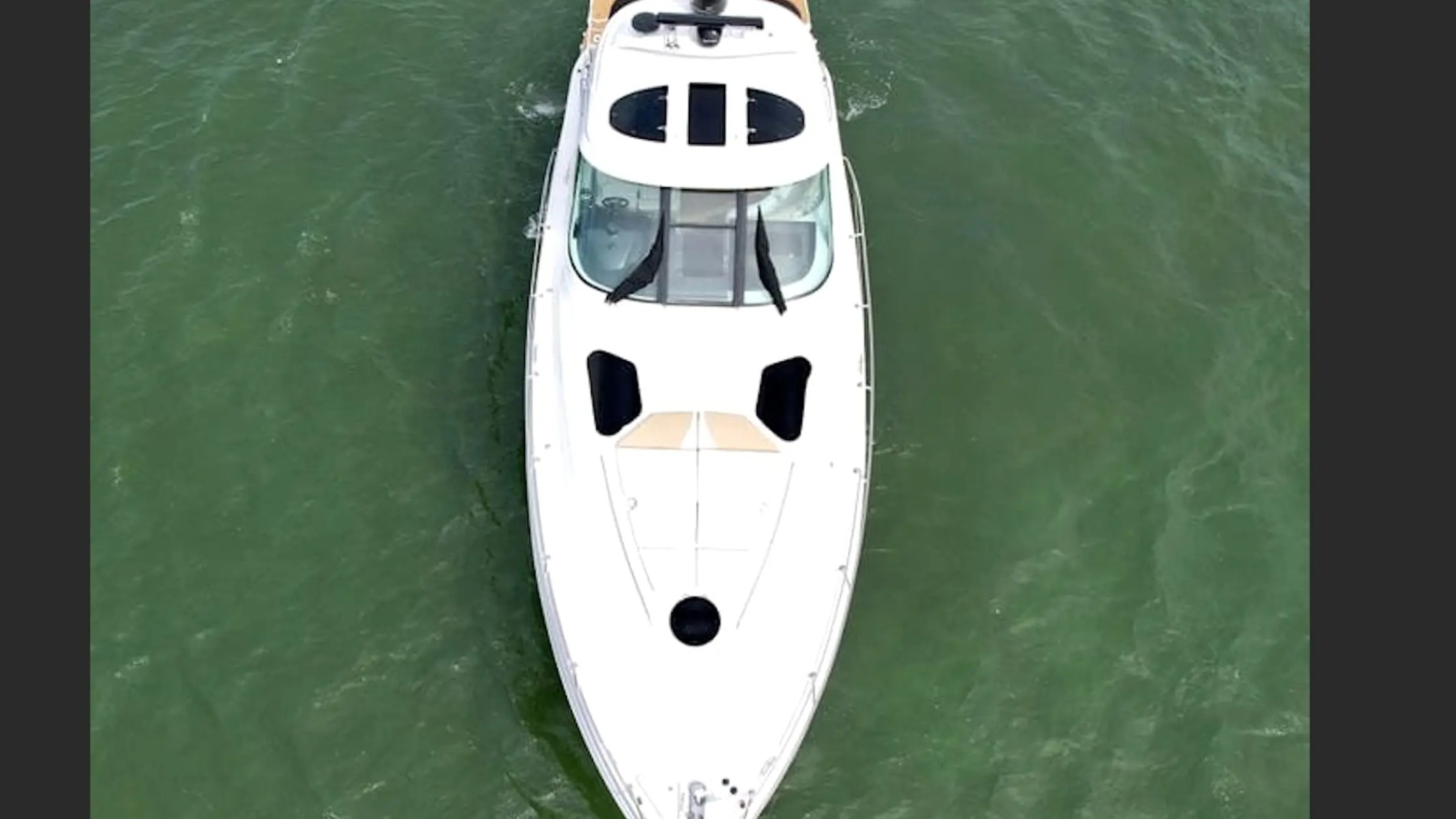 Aerial view of a white boat anchored in green water.
