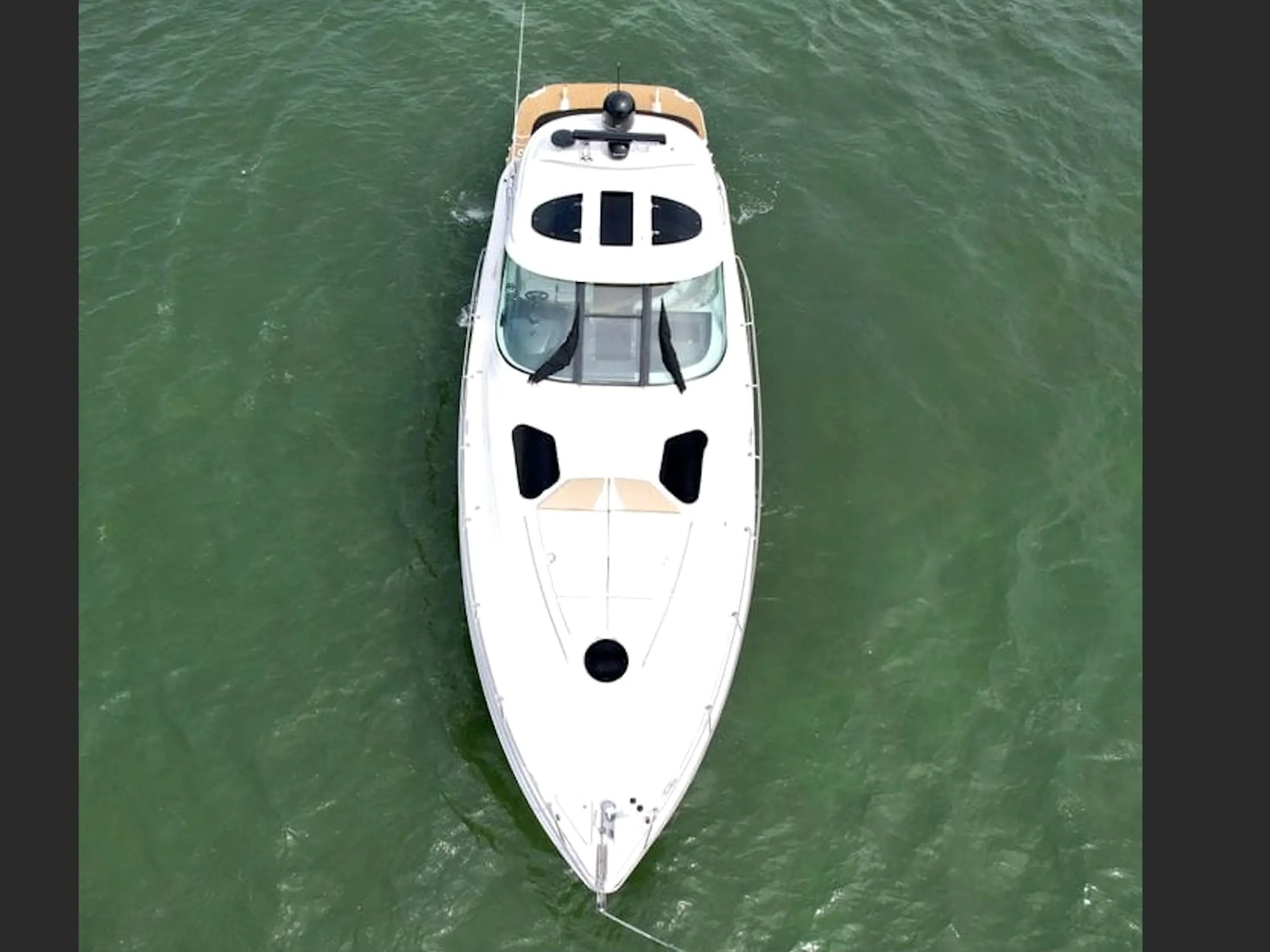 Aerial view of a white boat anchored in green water.