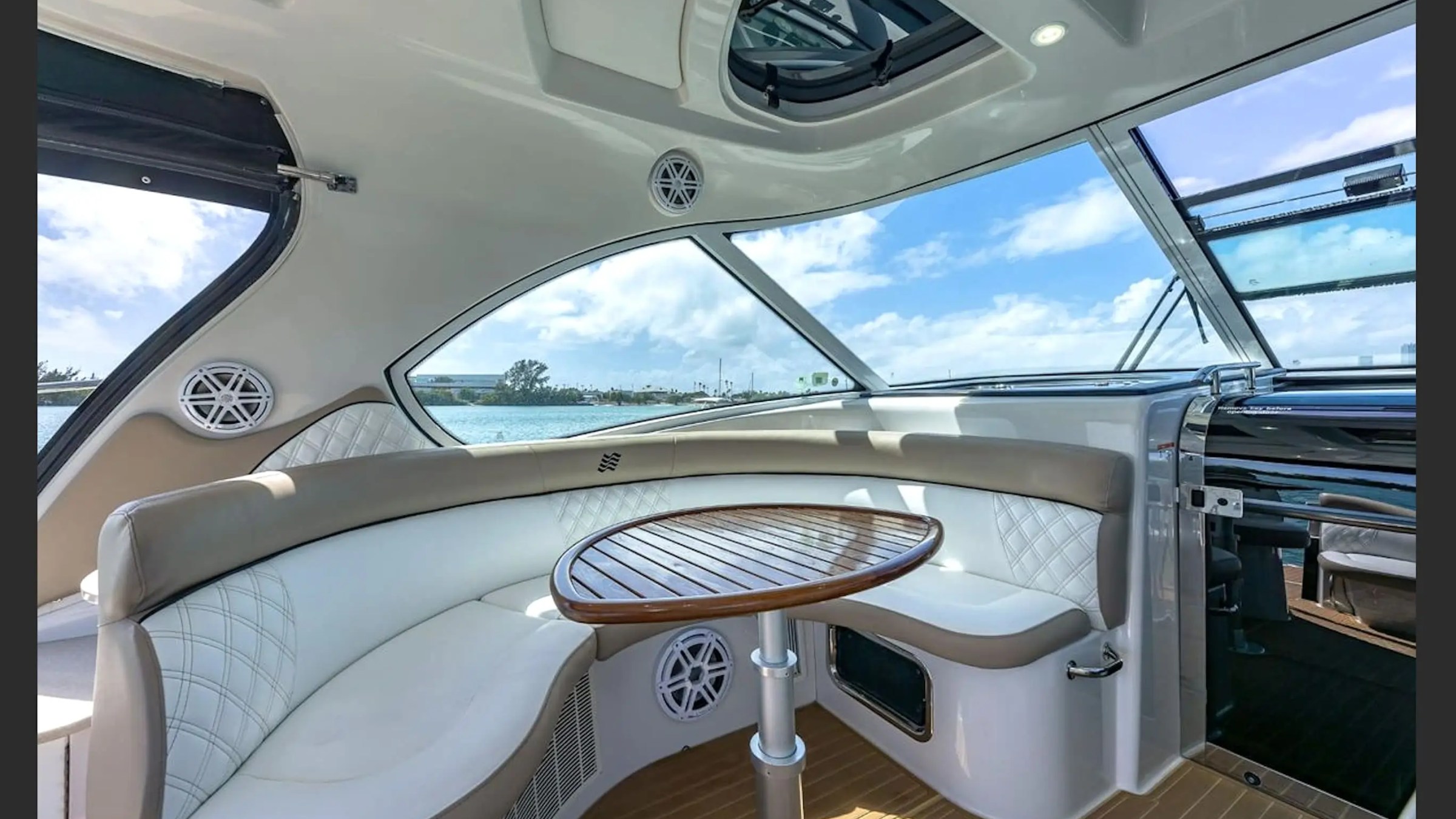 Luxury yacht interior with curved seating, wooden table, and large windows showing a view of the sky and sea.