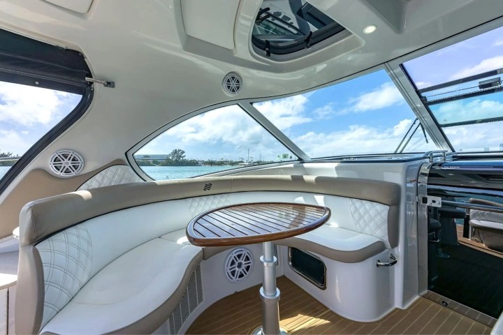 Luxury yacht interior with curved seating, wooden table, and large windows showing a view of the sky and sea.