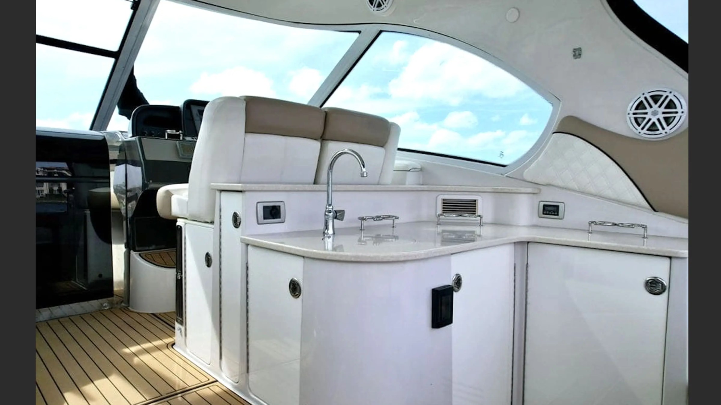 Luxurious boat interior with white cabinets, sink, and large windows showing a cloudy sky.