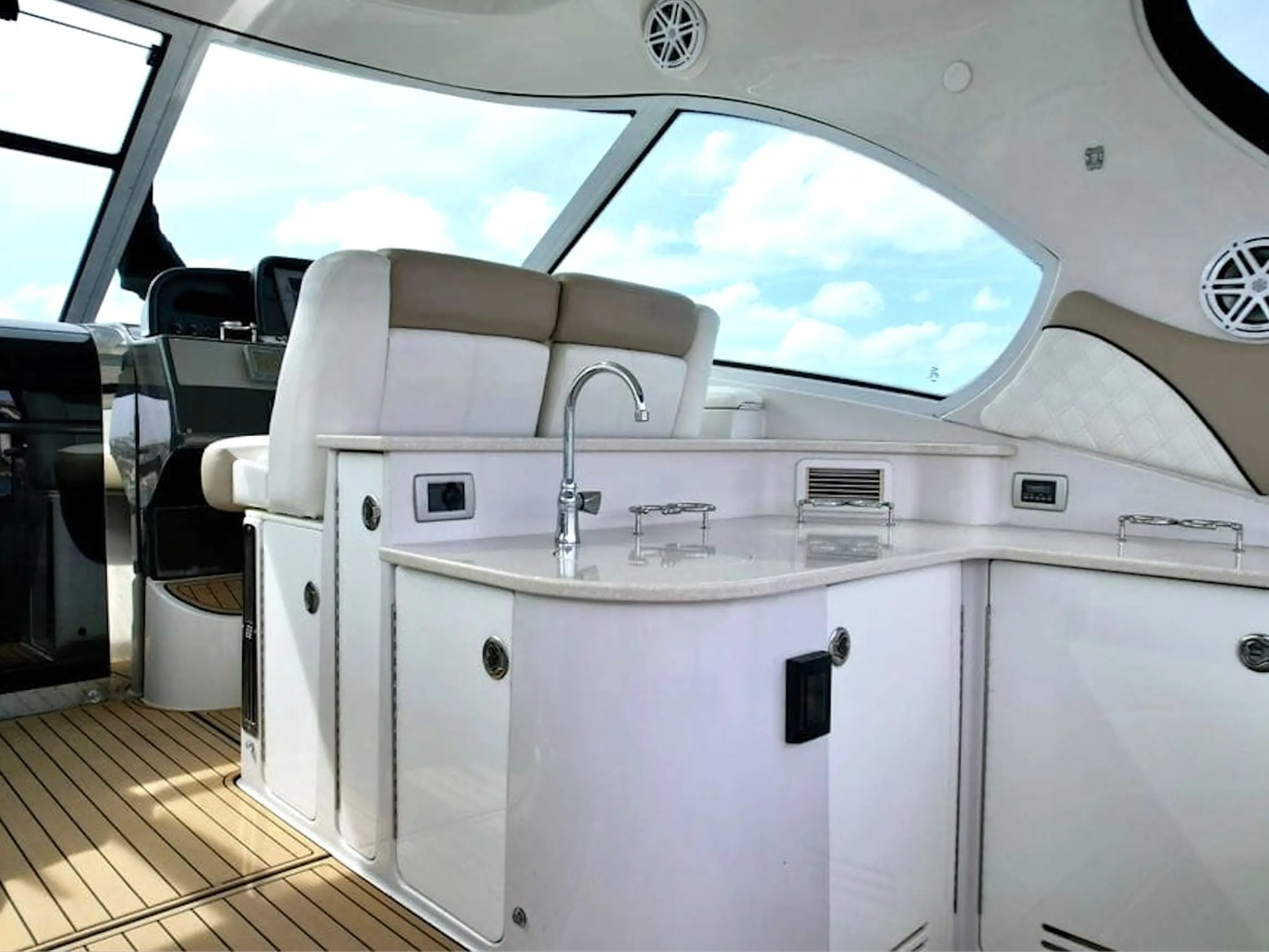 Luxurious boat interior with white cabinets, sink, and large windows showing a cloudy sky.
