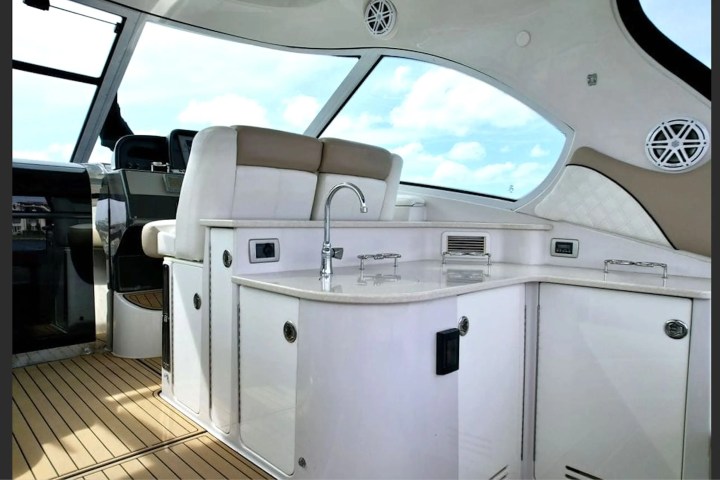 Luxurious boat interior with white cabinets, sink, and large windows showing a cloudy sky.