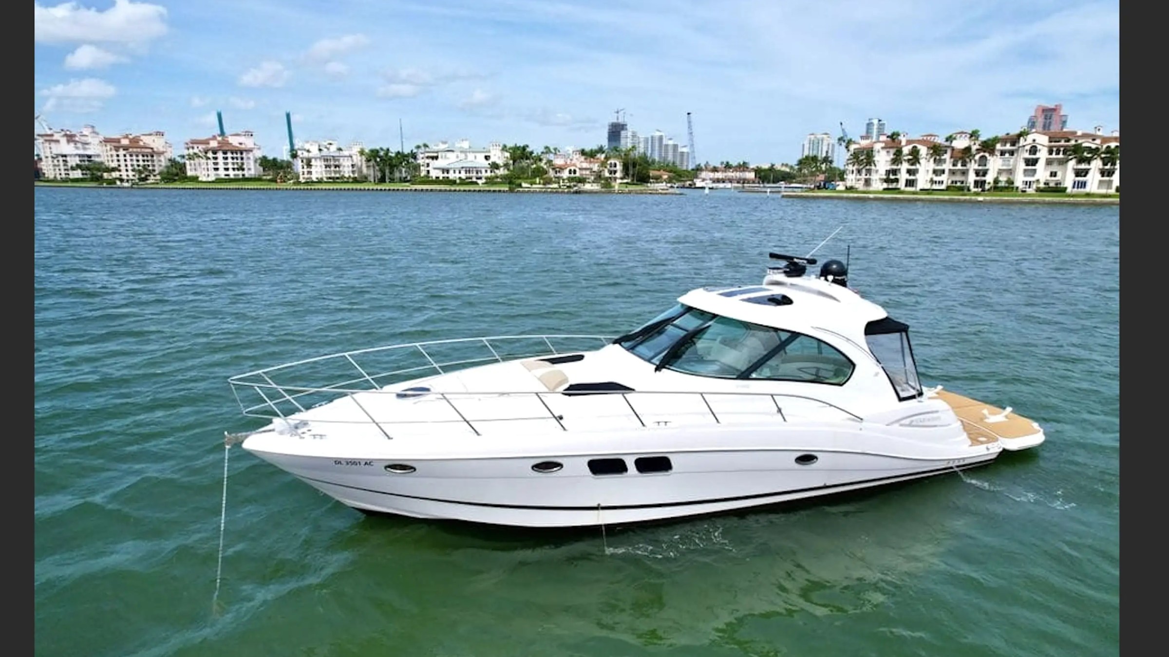 White yacht moored on calm water with cityscape and blue sky in the background.