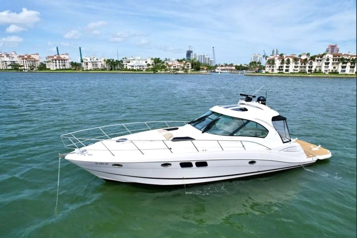 White yacht moored on calm water with cityscape and blue sky in the background.