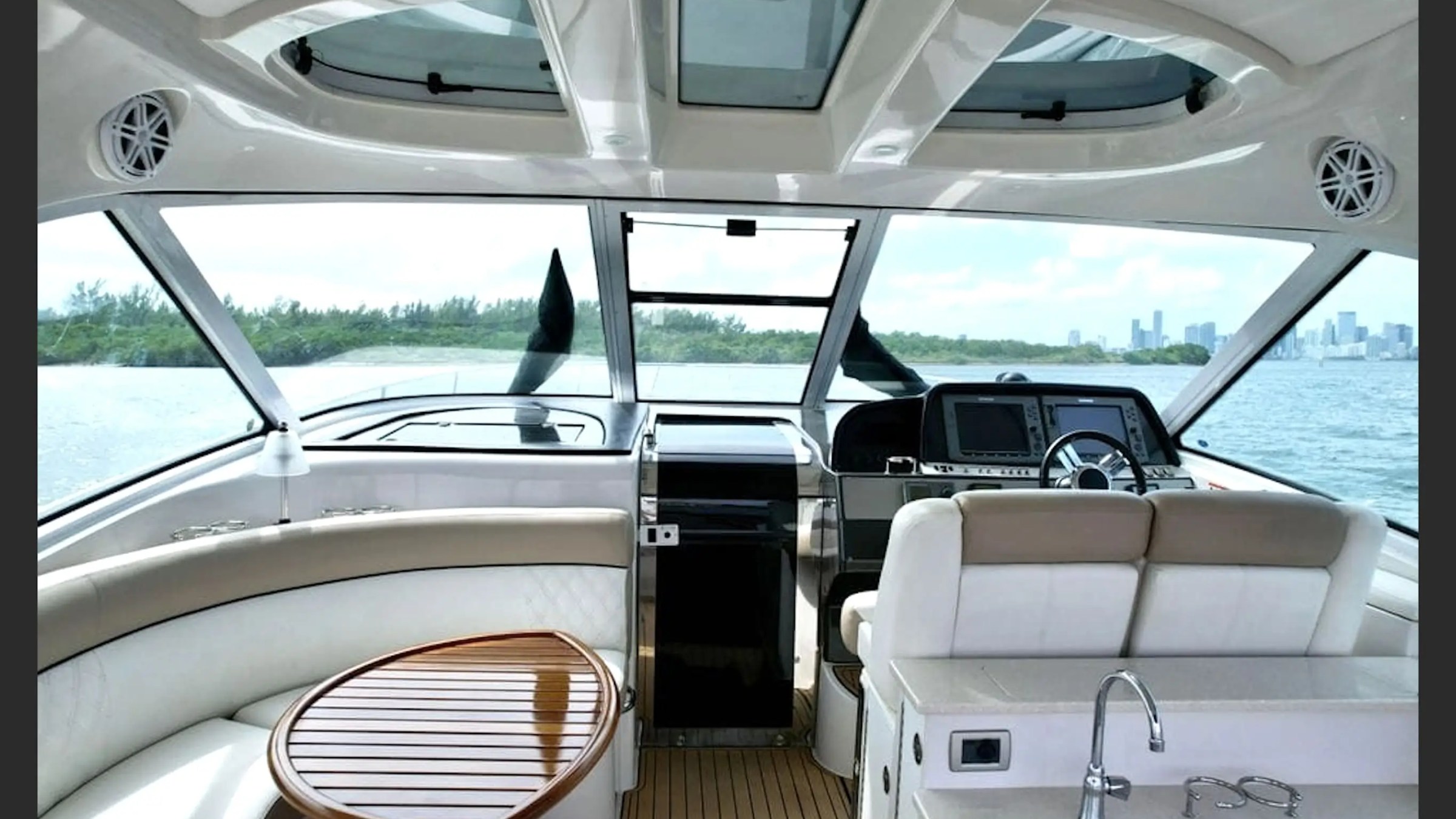 Interior of a yacht cockpit with steering wheel, seating, and water view.