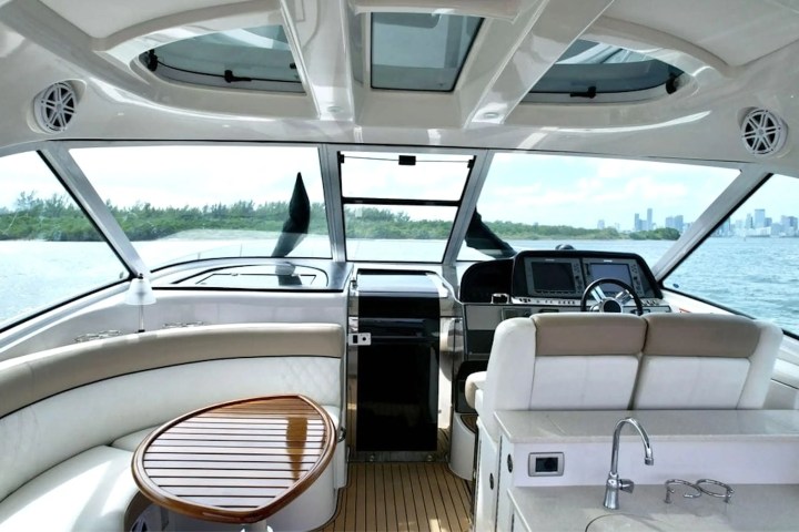 Interior of a yacht cockpit with steering wheel, seating, and water view.