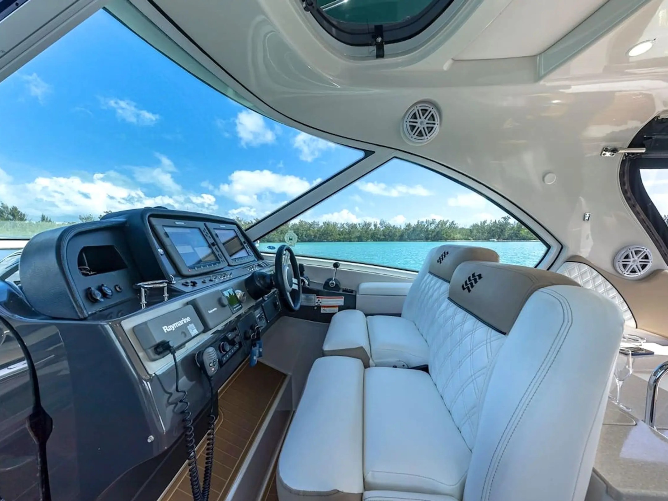 Interior of a boat cockpit with steering wheel, modern controls, and white seats.