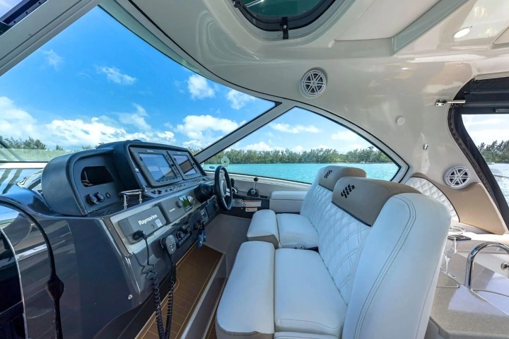 Interior of a boat cockpit with steering wheel, modern controls, and white seats.