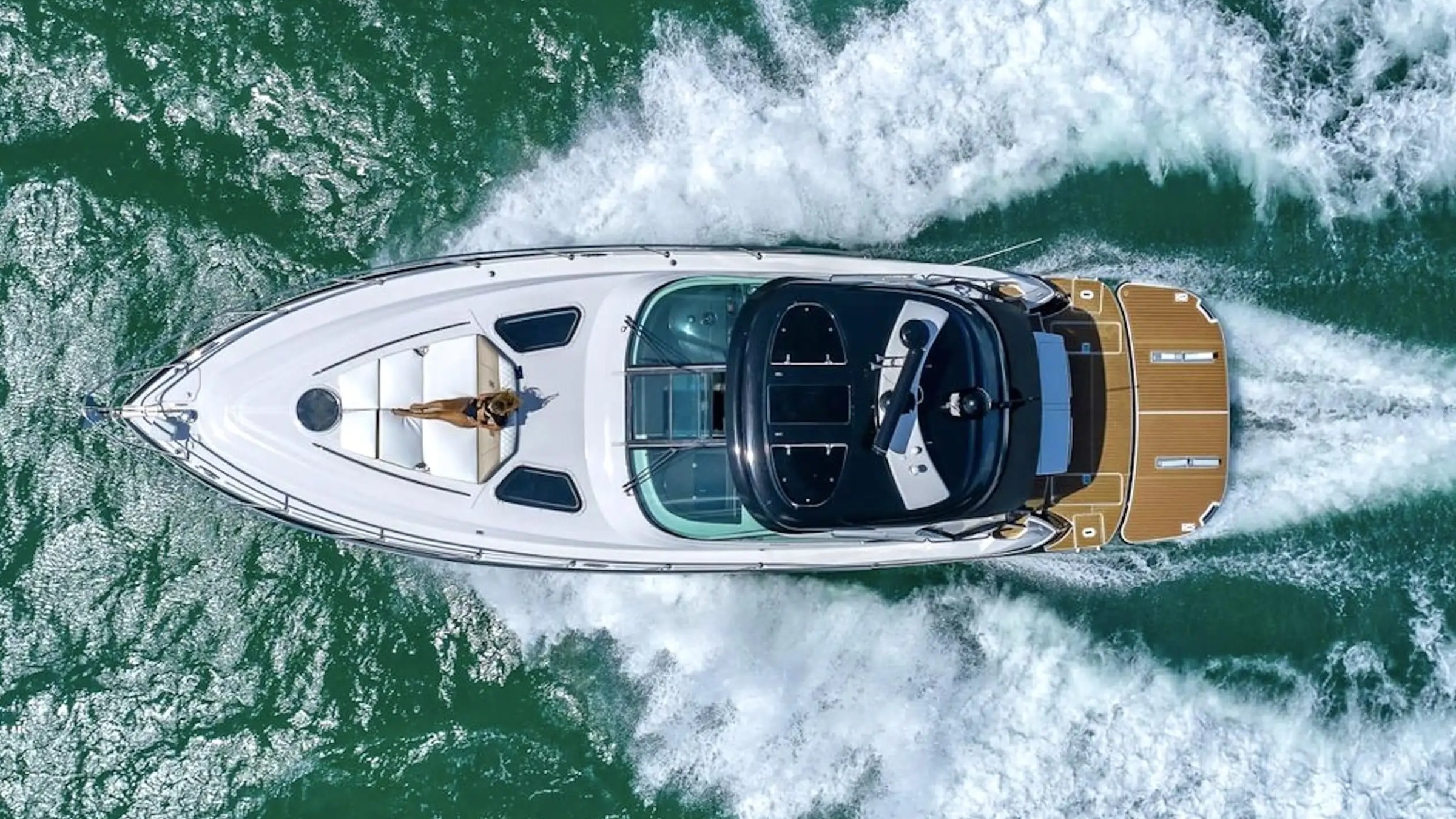 Aerial view of a white yacht speeding on the sea, leaving a trail of waves.