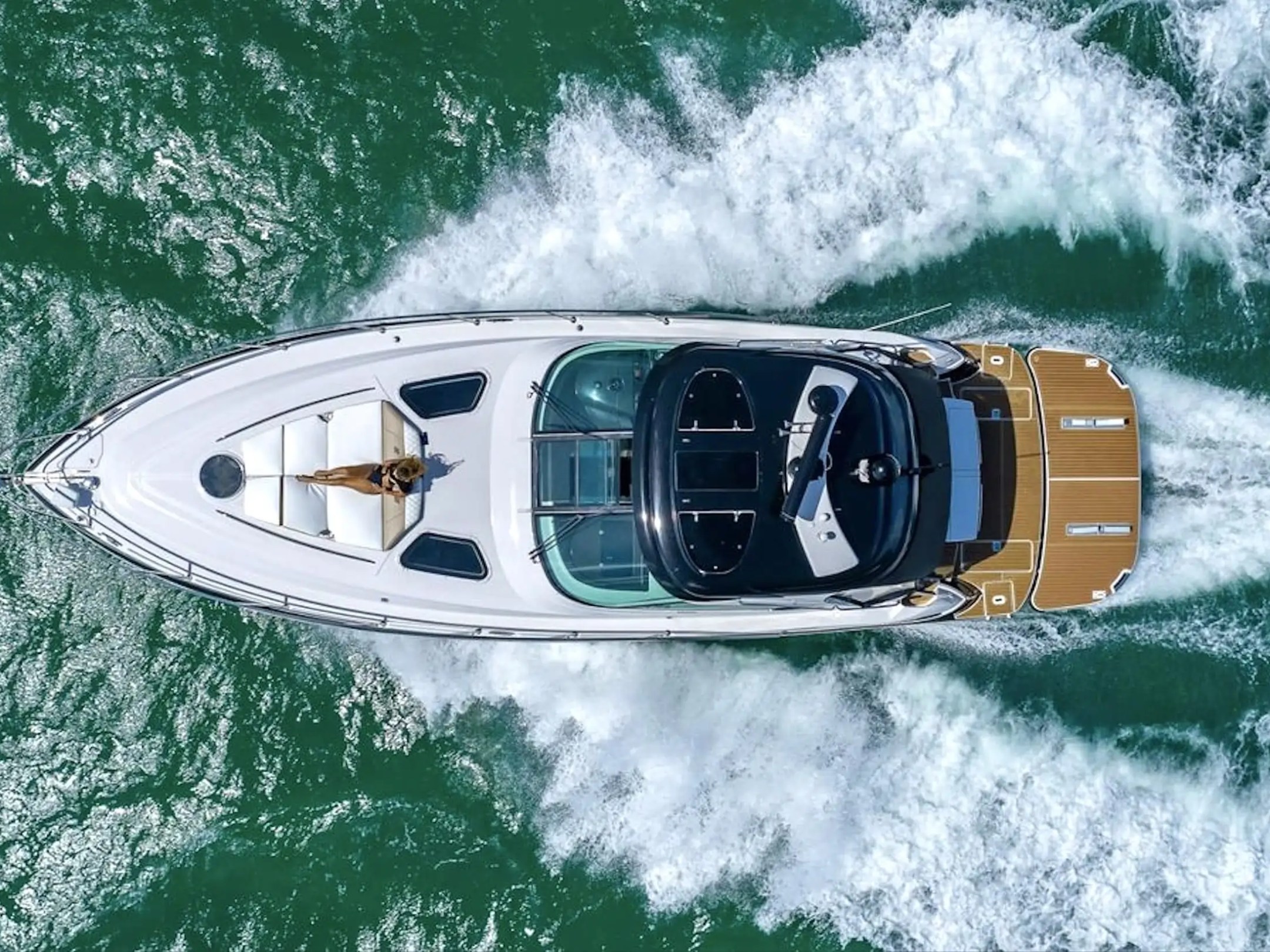 Aerial view of a white yacht speeding on the sea, leaving a trail of waves.