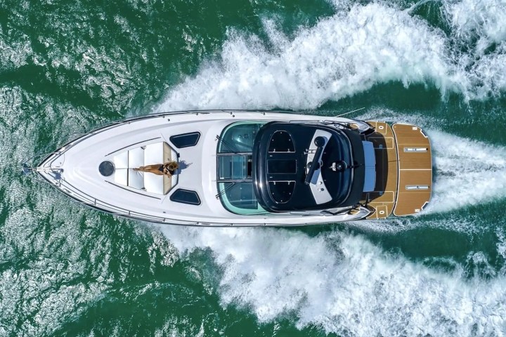 Aerial view of a white yacht speeding on the sea, leaving a trail of waves.