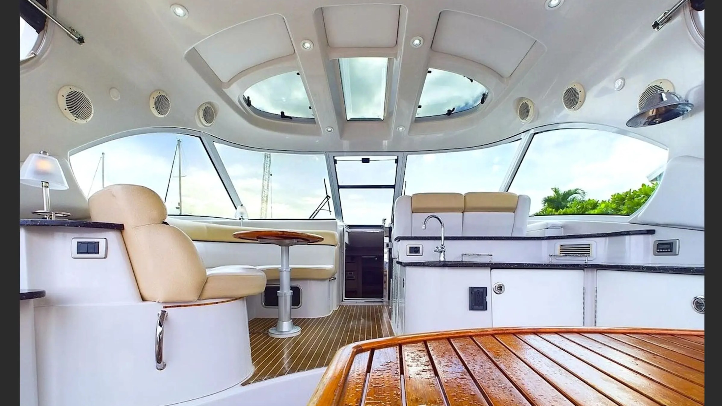 Interior of a yacht featuring beige seating, a small table, and a kitchen area with windows and skylights.