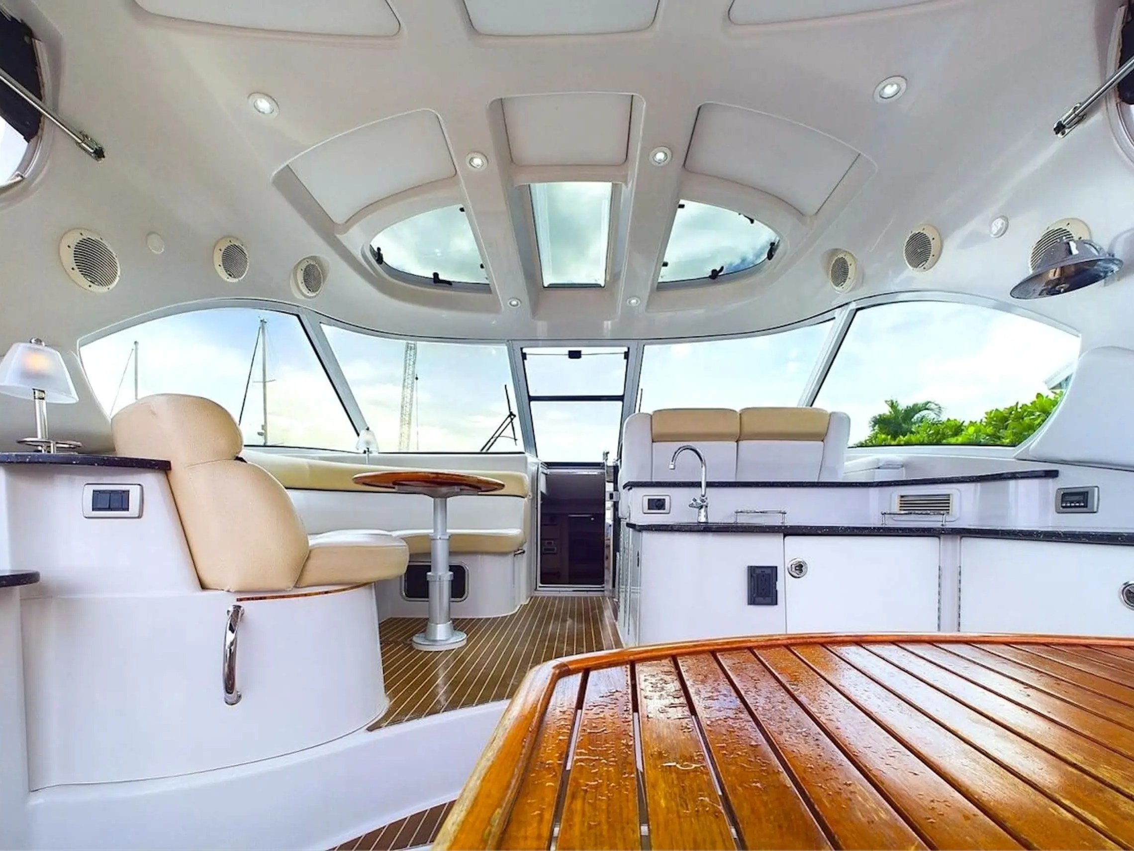 Interior of a yacht featuring beige seating, a small table, and a kitchen area with windows and skylights.