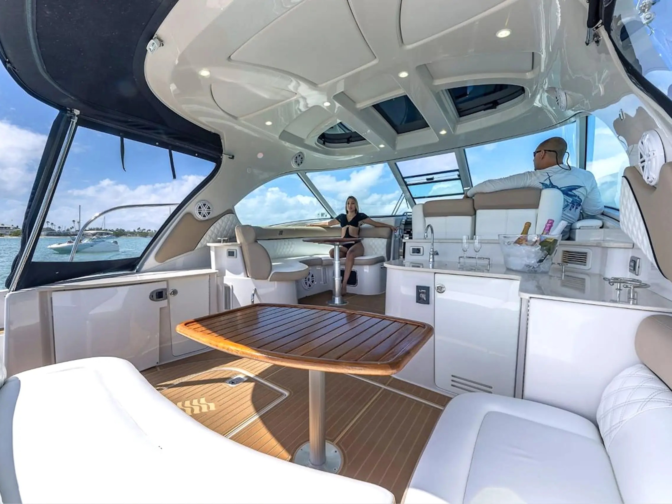People relaxing on a yacht with a wooden table and open canopy view of the water.