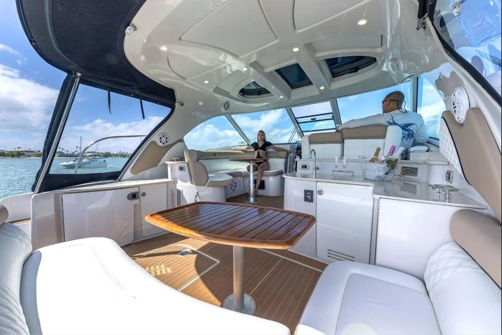 People relaxing on a yacht with a wooden table and open canopy view of the water.