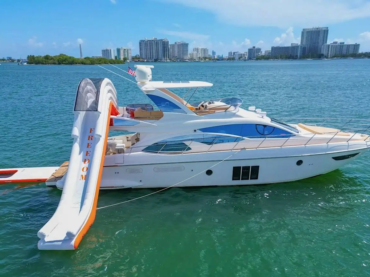 Luxury yacht with an inflatable slide on water, city skyline in background.