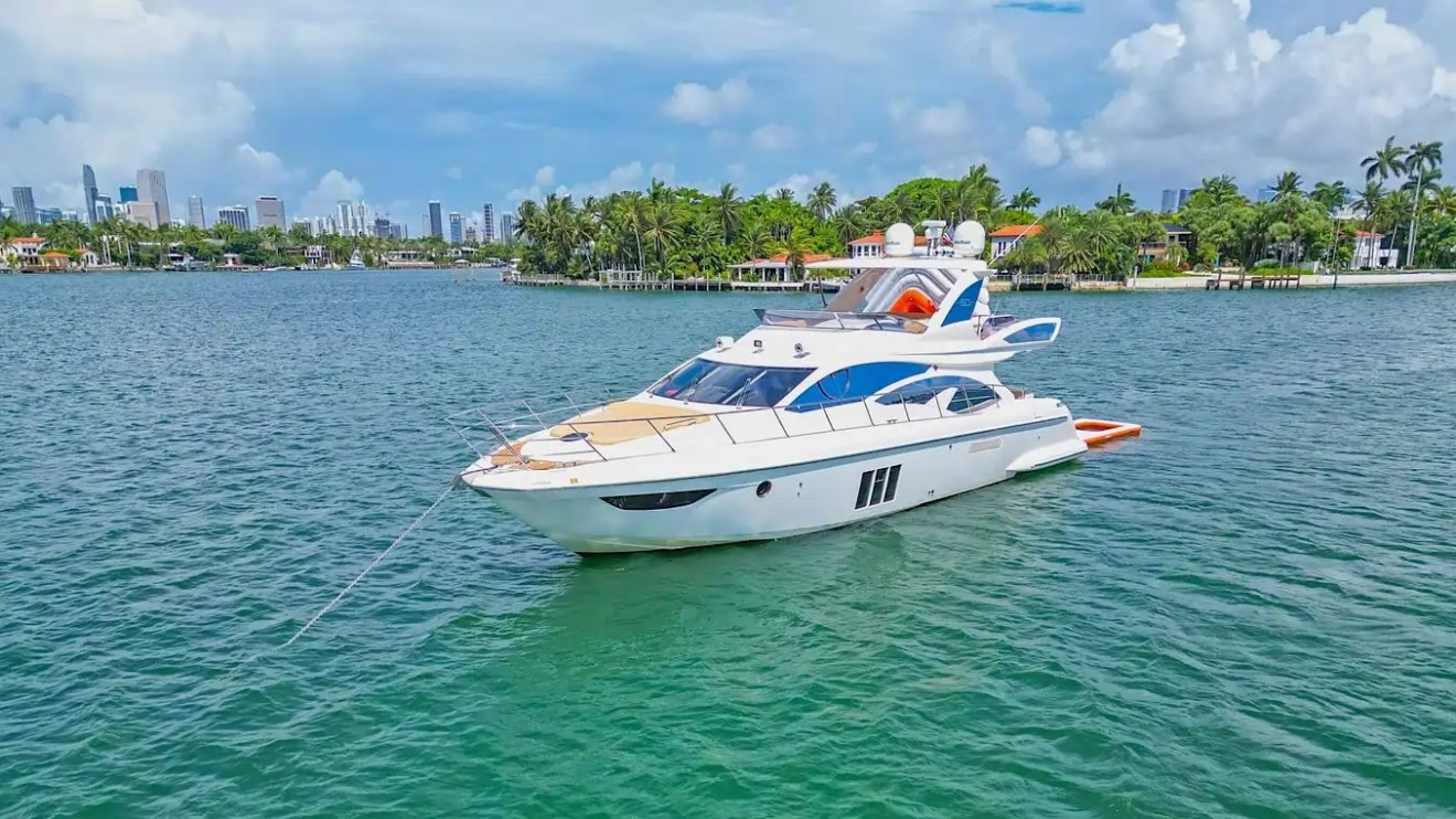 Luxury yacht anchored in a tropical bay with city skyline and palm trees in the background.