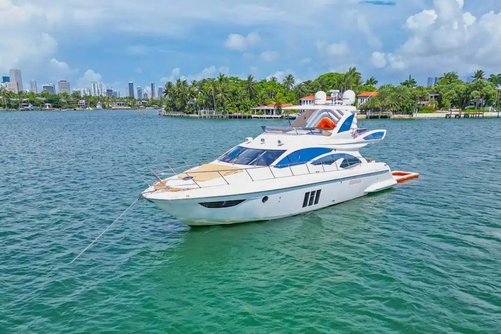 Luxury yacht anchored in a tropical bay with city skyline and palm trees in the background.
