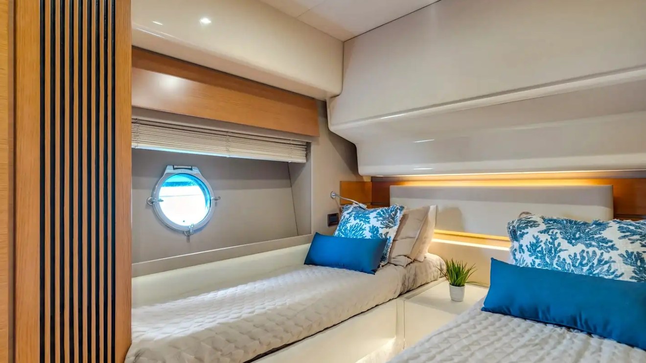 Cozy yacht bedroom with two beds, porthole, and decorative pillows.