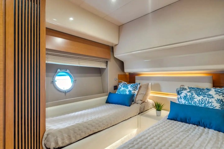 Cozy yacht bedroom with two beds, porthole, and decorative pillows.