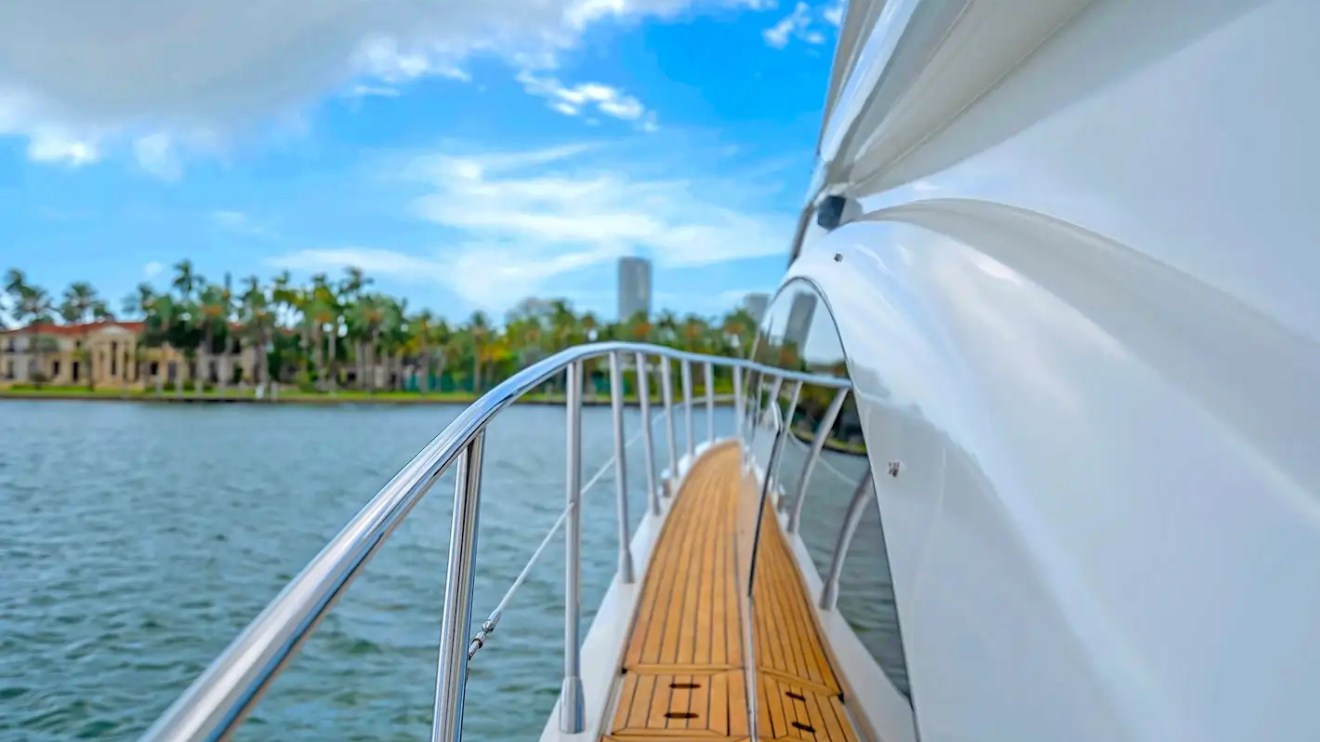 View from a yacht deck with railing, overlooking water and palm trees under a blue sky.