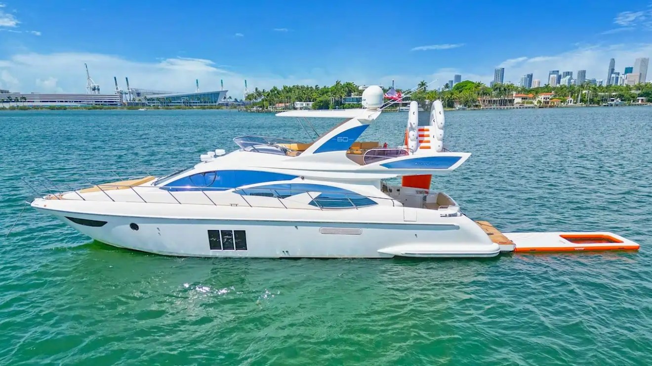 Luxury yacht on calm water with city skyline and clear blue sky in the background.