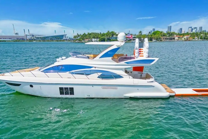 Luxury yacht on calm water with city skyline and clear blue sky in the background.