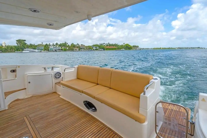 Rear view of boat deck with seating, overlooking water and shoreline with houses and trees.