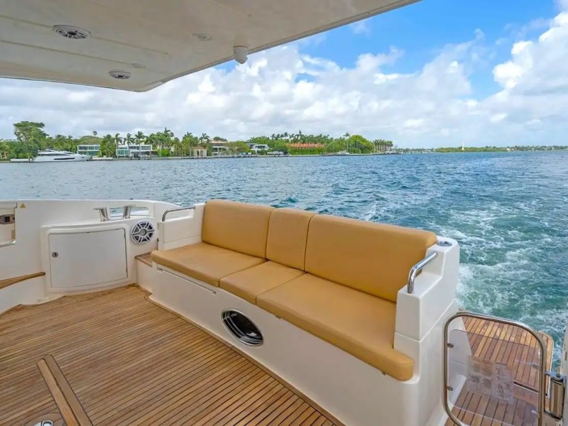Rear view of boat deck with seating, overlooking water and shoreline with houses and trees.