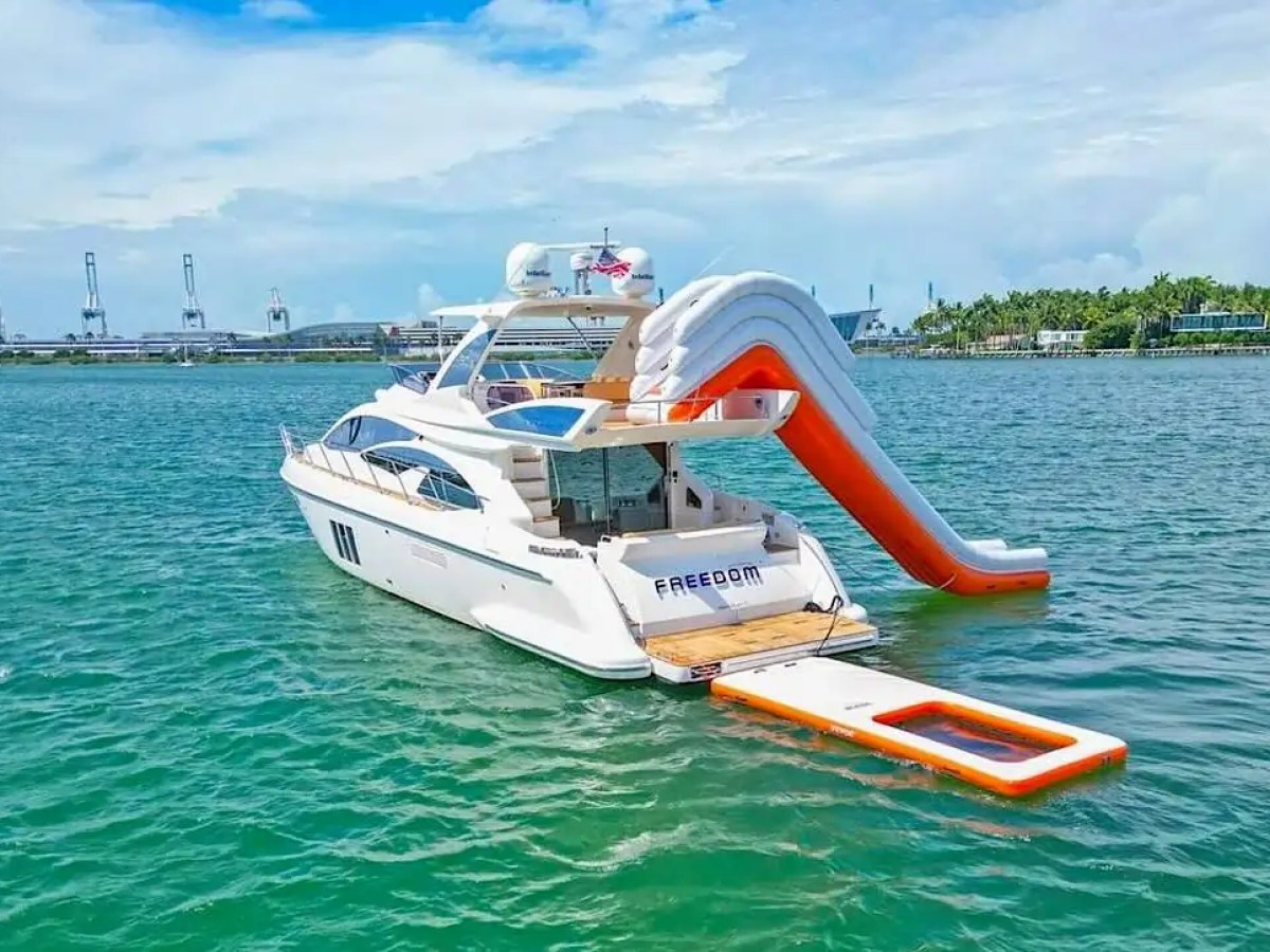 Luxury yacht with a slide and float on calm ocean near a coastline.