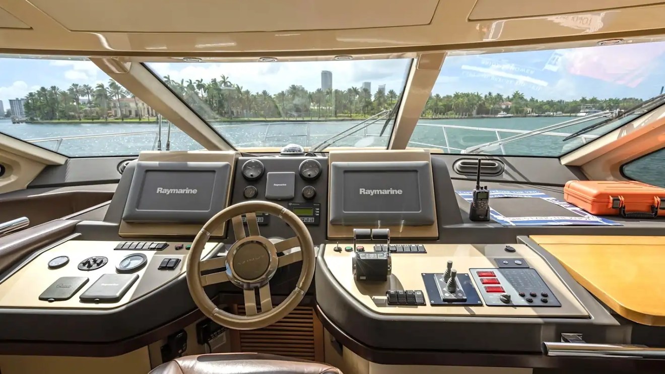 Luxury yacht cockpit with steering wheel, navigation screens, and sea view through large windows.