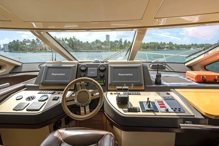 Luxury yacht cockpit with steering wheel, navigation screens, and sea view through large windows.