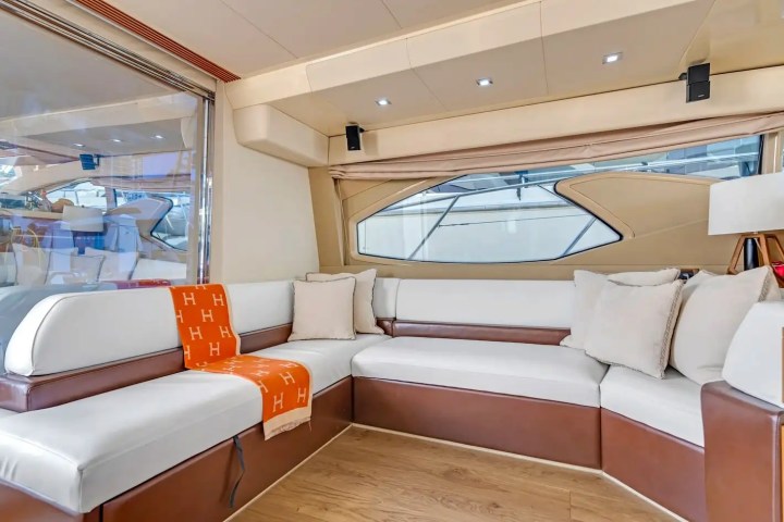 Luxury yacht interior with white and brown L-shaped sofa and orange blanket.