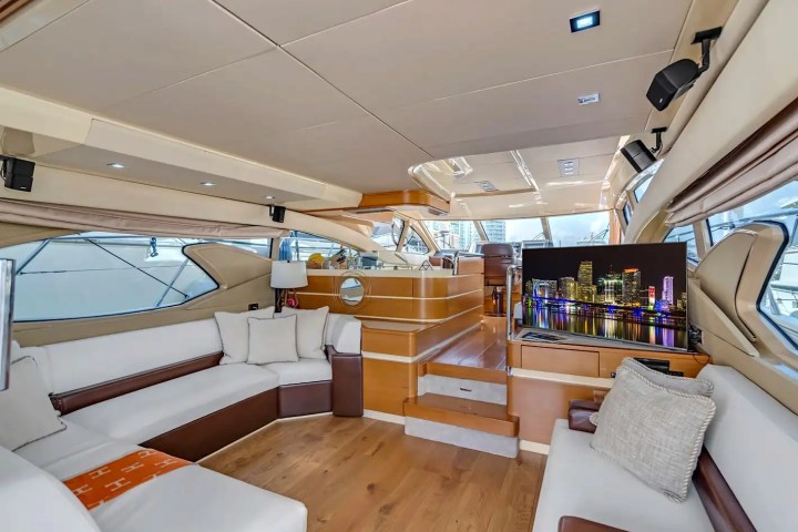 Luxurious yacht interior with white sofas, wood flooring, and a large TV.