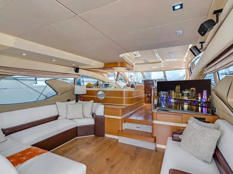 Luxurious yacht interior with white sofas, wood flooring, and a large TV.