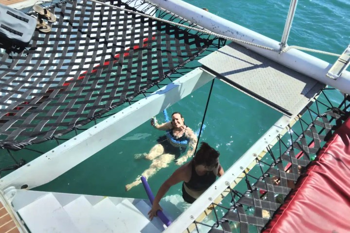 Two people swim near a boat with netted decks over the ocean.