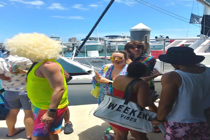 Group of people in colorful outfits near a docked boat under a bright blue sky.