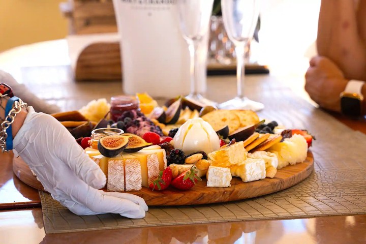 Charcuterie board with cheese, fruits, crackers, and hand placing it on a table.